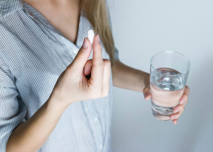 Close-up of a woman holding a pill and a glass of water, ready to take medication.